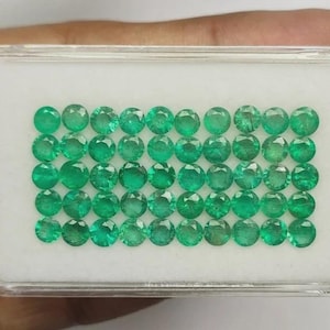 May include: A rectangular clear plastic display case containing forty small, round, faceted green emerald gemstones arranged in a grid of five rows and eight columns, set against a plain white foam insert background for clear visibility.