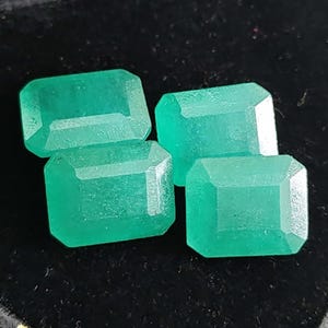 Pode incluir: Quatro pedras preciosas de esmeralda soltas com uma cor verde vibrante e um corte esmeralda retangular. Cada pedra apresenta superfícies facetadas que refletem a luz, exibindo uma aparência clara e polida com saturação consistente em todas.