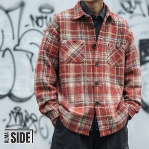 Peut inclure: Une chemise à manches longues boutonnée avec un motif à carreaux rouge, beige et gris. La chemise présente un col classique, deux poches poitrine et des boutons foncés. Le texte ALMA SIDE PRINTS est visible dans le coin inférieur gauche.