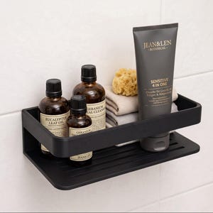 Peut inclure: Une étagère de douche rectangulaire noir mat contenant deux flacons en verre ambré étiquetés Eucalyptus Leaf Oil et Geranium Facial Cleanser, un grand tube de soin Jean & Len Sensitive 4 in One, un gant de toilette beige et une éponge naturelle.