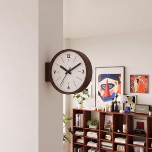 Pode incluir: Um relógio de parede de face dupla com uma moldura circular castanho-escura e um mostrador branco. O relógio apresenta ponteiros pretos para as horas e minutos, marcas pretas finas para cada hora e os números 12, 3, 6 e 9 impressos.