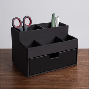 Könnte beinhalten: Ein mattschwarzer Schreibtisch-Organizer mit abgestuftem Design, mehreren Fächern und einer ausziehbaren Schublade. Der obere Bereich enthält eine Schere mit roten Akzenten, einen grünen Stift und einen silbernen Stift zur Aufbewahrung von Büroartikeln.