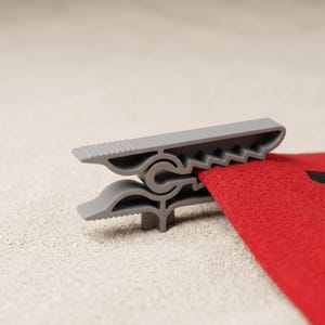 Op de afbeelding: Een grijze plastic wasknijper met een getextureerd greepgedeelte en een gekarteld ontwerp aan de binnenkant van de kaken. De knijper staat in een horizontale positie en houdt stevig een stuk rode stof vast tussen de kaken.
