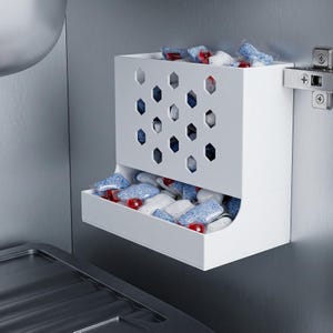 Peut inclure: Un conteneur de rangement blanc, mural, avec un motif géométrique, rempli de dosettes de détergent bleues, blanches et rouges. Le conteneur a un tiroir pour un accès facile et est fixé à une surface en acier inoxydable.