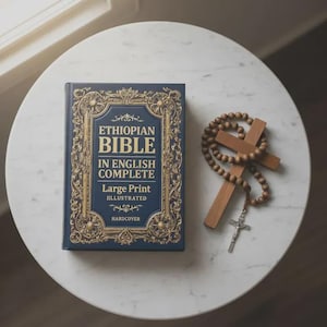 Op de afbeelding: Een donkerblauwe hardcover "Ethiopische Bijbel in het Engels Compleet" met gouden details en grote letters. Een houten kruis en rozenkrans liggen naast het boek op een wit marmeren oppervlak.