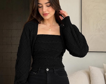 May include: Black knitwear set featuring a square-neck tube top and a matching cardigan with diamond-patterned sleeves. The set is paired with black jeans. The outfit is a stylish ensemble, perfect for a casual or semi-formal occasion.