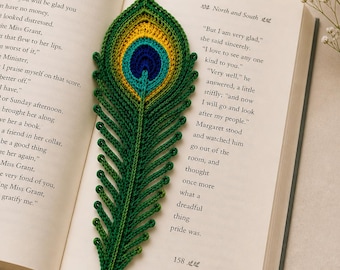 May include: A handmade crochet bookmark shaped like a peacock feather. The bookmark features a vibrant color palette of green, yellow, blue, and navy, and is placed inside an open book. The bookmark is a unique accessory for book lovers.