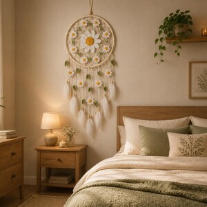Puede incluir: Una escena de dormitorio con un atrapasue&ntilde;os con dise&ntilde;o de margarita sobre una cama. La habitaci&oacute;n presenta muebles de madera, incluyendo una mesita de noche y una c&oacute;moda. La cama est&aacute; adornada con almohadas y una manta verde, creando un ambiente relajante.