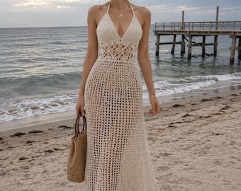 May include: A floor-length, cream-colored crochet dress featuring a halter neckline, a fitted bodice with intricate openwork patterns, and a flared skirt with a detailed scalloped hem. The garment is constructed from a lightweight, woven yarn.