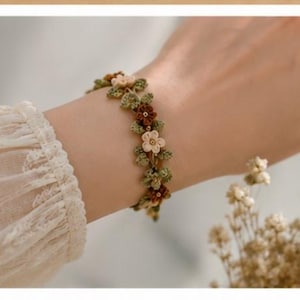 May include: A floral bracelet featuring small, cream-colored and burgundy flowers with green leaves. The bracelet is worn on a wrist, with a cream-colored, lace-trimmed sleeve visible.