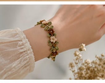 May include: A floral bracelet featuring small, cream-colored and burgundy flowers with green leaves. The bracelet is worn on a wrist, with a cream-colored, lace-trimmed sleeve visible.
