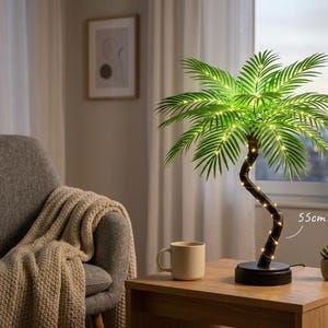 May include: A decorative palm tree lamp with a curved brown trunk and green fronds, illuminated by small lights. The lamp is 21.6 inches tall and sits on a black base. A small succulent and a mug are on the wooden table.