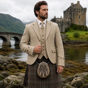 Può includere: Un blazer in tweed beige e un gilet abbinato indossati sopra una camicia bianca con colletto e cravatta, abbinati a un kilt scozzese e uno sporran rifinito in pelliccia con dettagli in metallo. L'insieme presenta bottoni marroni sui polsini.