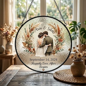 Könnte beinhalten: Runde Hochzeitsdekoration aus Glas mit schwarzem Metallrahmen und Kette. Das Bild zeigt ein sich umarmendes Paar, umgeben von floralen Elementen. Text: "Aria & Silas", "September 14, 2024" und "Happily Ever After Begins."