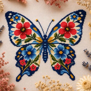 May include: A cross-stitch embroidery pattern on white fabric featuring a large butterfly with blue, red, and yellow floral motifs. The butterfly wings are detailed with symmetrical red and blue flowers, green leaves, and yellow accents.