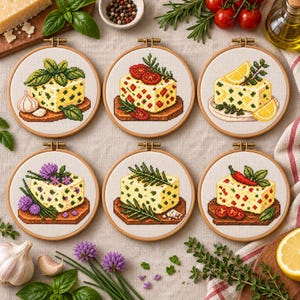 May include: Six circular wooden embroidery hoops containing cross-stitch patterns of cheese blocks. Each block is garnished with different ingredients including basil, garlic, tomatoes, lemon slices, chives, rosemary, and chilli peppers on a fabric background.