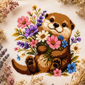 Puede incluir: Un bordado de punto de cruz sobre tela blanca que muestra una nutria marrón sosteniendo un ramo de flores coloridas. El arreglo floral incluye cosmos rosas, margaritas blancas, lavanda morada y pequeñas flores azules, todo en puntadas detalladas.