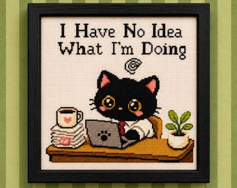 Puede incluir: Un bordado en punto de cruz enmarcado que muestra un gato negro sentado en un escritorio con un portátil, una pila de papeles, una taza de café y una pequeña planta en maceta. El texto sobre el gato dice I Have No Idea What I'm Doing.