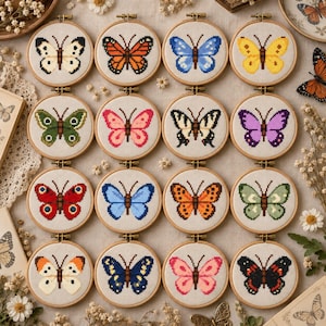 May include: A collection of sixteen circular wooden embroidery hoops, each featuring a unique cross-stitch butterfly design in various colors including orange, blue, yellow, green, pink, red, and black, displayed on a neutral fabric background.