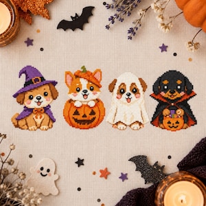 Puede incluir: Un patrón de punto de cruz sobre tela clara que muestra cuatro cachorros con disfraces de Halloween: un perro con sombrero de bruja y capa morada, un corgi dentro de una calabaza, un cachorro de fantasma y un perro negro de vampiro.