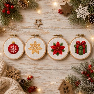 May include: Four circular wooden embroidery hoops containing cross-stitch designs on white fabric. The designs feature a red Christmas ornament, a gold star, a red poinsettia flower, and a green gift box with a red bow, arranged horizontally.