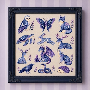 May include: A framed cross-stitch embroidery featuring a grid of twelve animals and insects in shades of blue and purple. The collection includes an owl, butterfly, fox, turtle, rabbit, deer, dragon, wolf, raven, snake, and hedgehog, all adorned with crescent moon motifs.