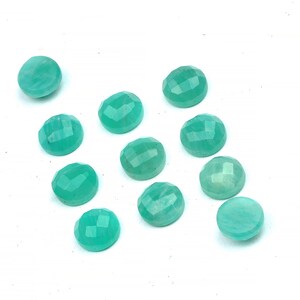 Peut inclure: Douze pierres pr&eacute;cieuses rondes, facett&eacute;es, de couleur vert turquoise. Les pierres pr&eacute;cieuses sont dispos&eacute;es en un motif l&acirc;che et dispers&eacute; sur une surface blanche.