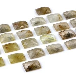 May include: A collection of 20 clear quartz cabochons with golden rutile inclusions. The cabochons are rectangular in shape and have a smooth, polished finish.
