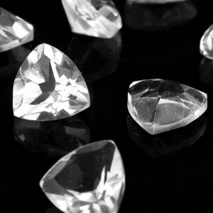 May include: A group of clear, triangular, faceted gemstones on a black background. The gemstones are arranged in a random pattern.
