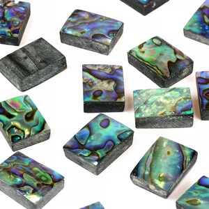 Puede incluir: Una colección de azulejos de concha de abulón iridiscente en varios tonos de verde, azul y morado. Los azulejos son rectangulares y tienen una superficie lisa y pulida.