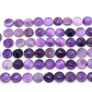 May include: A collection of 36 round, faceted amethyst gemstones. The stones are a deep purple color and have a smooth, polished finish.