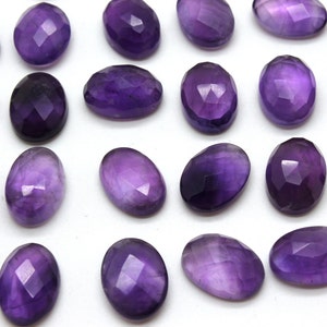May include: A collection of 20 faceted amethyst gemstones, each with a smooth, oval shape. The stones are a deep purple color and have a glossy finish.