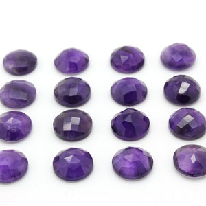 May include: A collection of 16 round, faceted amethyst gemstones. The stones are a deep purple color and are arranged in four rows of four.