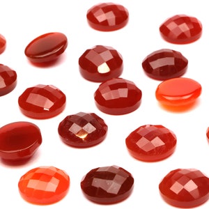 May include: A collection of 18 red carnelian cabochons, some with a faceted finish, arranged on a white background.
