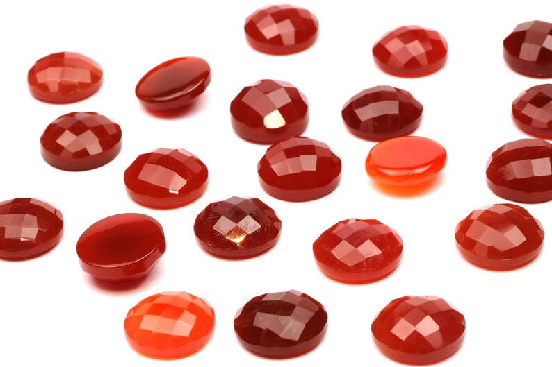 May include: A collection of 18 red carnelian cabochons, some with a faceted finish, arranged on a white background.