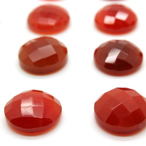 May include: A collection of 12 red carnelian gemstones, each with a faceted, rounded shape. The stones are arranged in rows on a white surface.