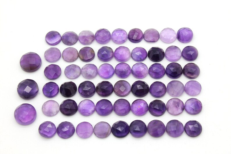 May include: A collection of 36 round, faceted amethyst gemstones. The stones are a deep purple color and have a smooth, polished finish.