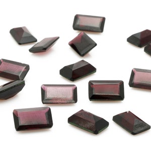 Puede incluir: Una colección de 15 piedras preciosas rectangulares de color púrpura oscuro y verde, esparcidas sobre un fondo blanco.