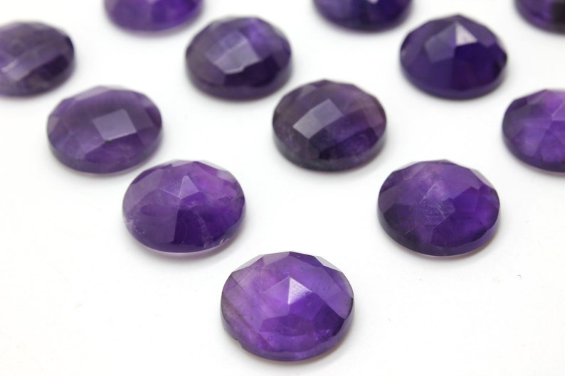 May include: A collection of twelve round, faceted amethyst gemstones. The gemstones are a deep purple color and have a smooth, polished finish.