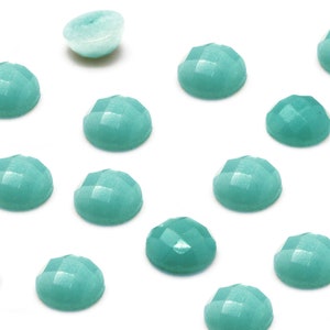 Peut inclure: Une collection de 14 pierres pr&eacute;cieuses cabochon vert turquoise, certaines sont rondes et d'autres l&eacute;g&egrave;rement ovales. Les pierres pr&eacute;cieuses sont dispos&eacute;es en un motif dispers&eacute; sur un fond blanc.