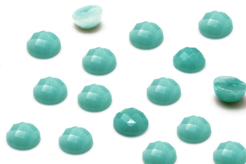Peut inclure: Une collection de 14 pierres pr&eacute;cieuses cabochon vert turquoise, certaines sont rondes et d'autres l&eacute;g&egrave;rement ovales. Les pierres pr&eacute;cieuses sont dispos&eacute;es en un motif dispers&eacute; sur un fond blanc.