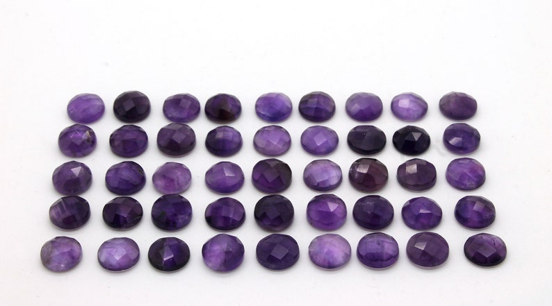 May include: A collection of 40 round, faceted amethyst gemstones. The stones are a deep purple color and are arranged in rows on a white background.
