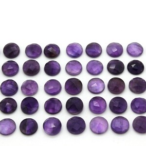 May include: A collection of 36 round, faceted amethyst gemstones. The stones are a deep purple color and are arranged in a grid pattern.