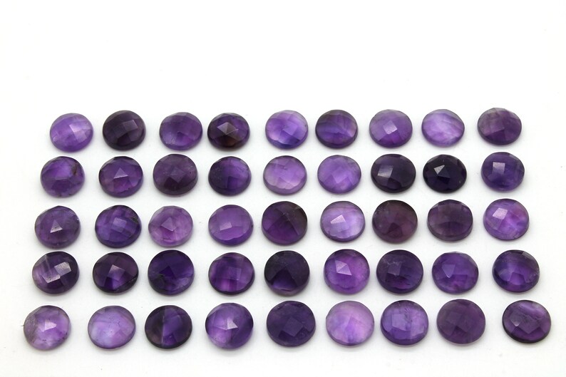May include: A collection of 36 round, faceted amethyst gemstones. The stones are a deep purple color and are arranged in a grid pattern.