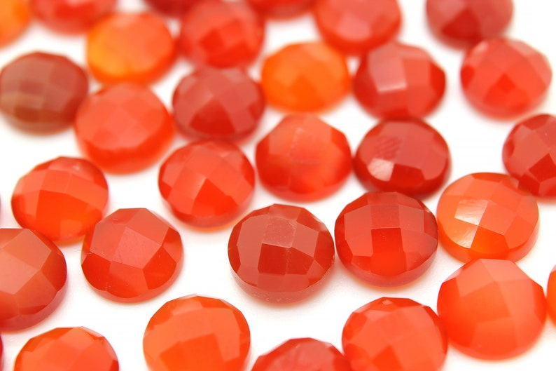 May include: A collection of smooth, round, red carnelian gemstones. The stones are faceted and have a polished finish.