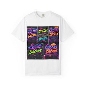 May include: White t-shirt featuring a colorful graphic design with the text "The Color of a Decade." The design includes images of a boombox, a car, a video game controller, and a retro video game console. The design has a retro 80s vibe.