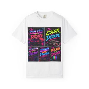 May include: White t-shirt featuring a colorful graphic design with the text "The Color of a Decade." The design includes images of a car, a video game controller, a radio, and a television, all in vibrant neon colors.