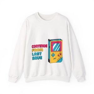 May include: White sweatshirt featuring a retro handheld video game console graphic. The text "CONTINUE FROM LAST SAVE" is printed in pink, yellow, and blue. The design is on the front of the sweatshirt.