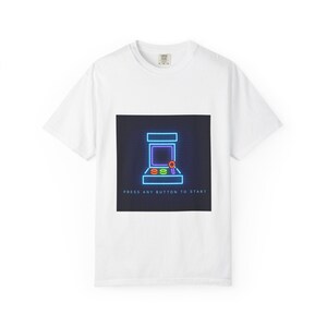 Op de afbeelding: Wit T-shirt met een neon arcade machine ontwerp op een zwarte vierkant. De arcade machine is omlijnd in blauw, paars en oranje. De tekst "PRESS ANY BUTTON TO START" staat eronder. Een klassiek T-shirt voor gamers.