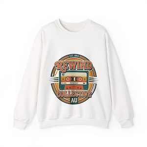 May include: White sweatshirt with a retro cassette tape design. The design includes the words "REWIND COLLECTIVE AU" and "EST. 1983" in a circular, vintage-style graphic. The cassette tape is in shades of brown, orange, and yellow.